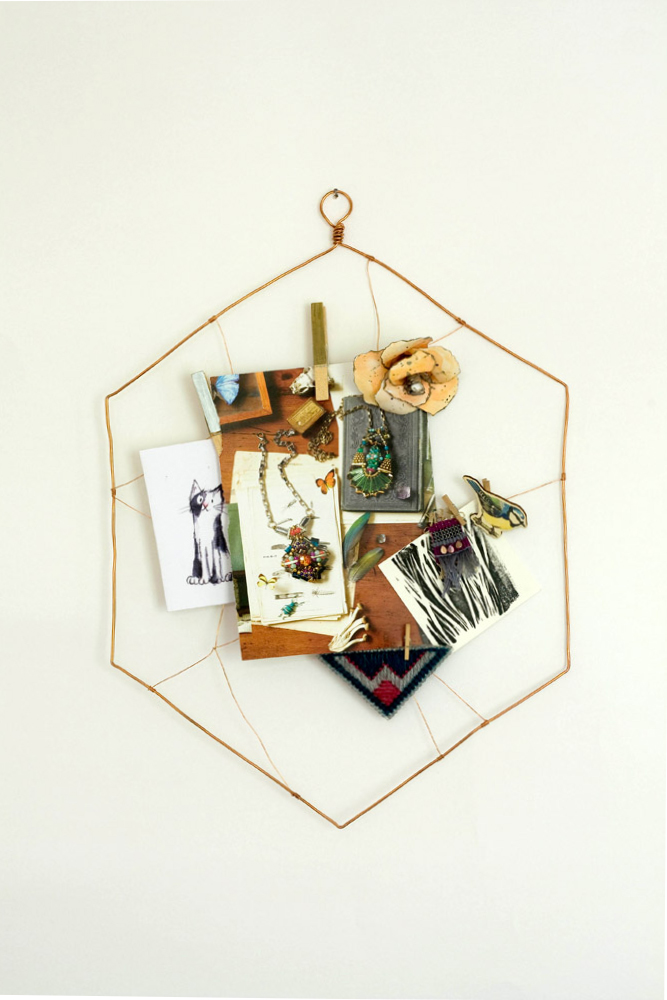 a wire memo board made from copper wire, complete with photos, illustrations and a paper flower attached to it on a white wall