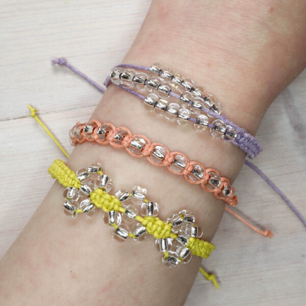 Finished Beaded macrame bracelet kit contents being worn on a white persons arm. There is a lilac, peach and yellow bracelet, each with shiny clear beads