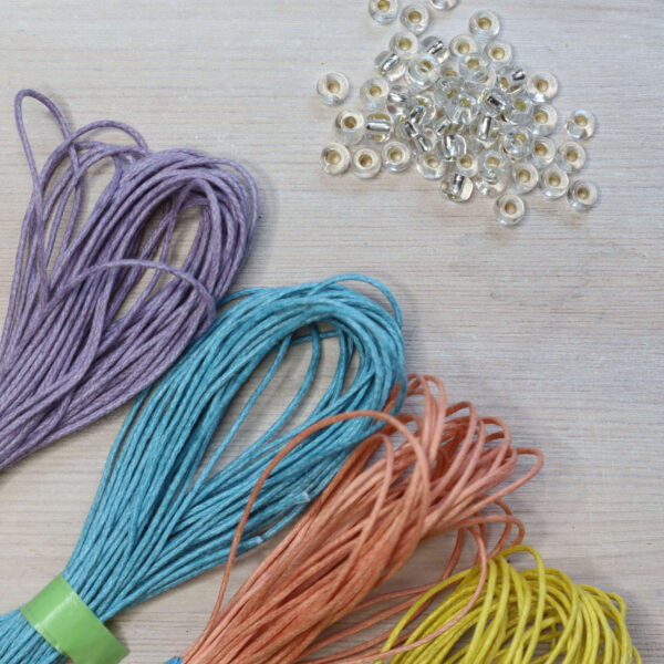 Beaded macrame bracelet kit contents, showing lilac, light blue, peach and yellow cotton cords with shiny clear beads