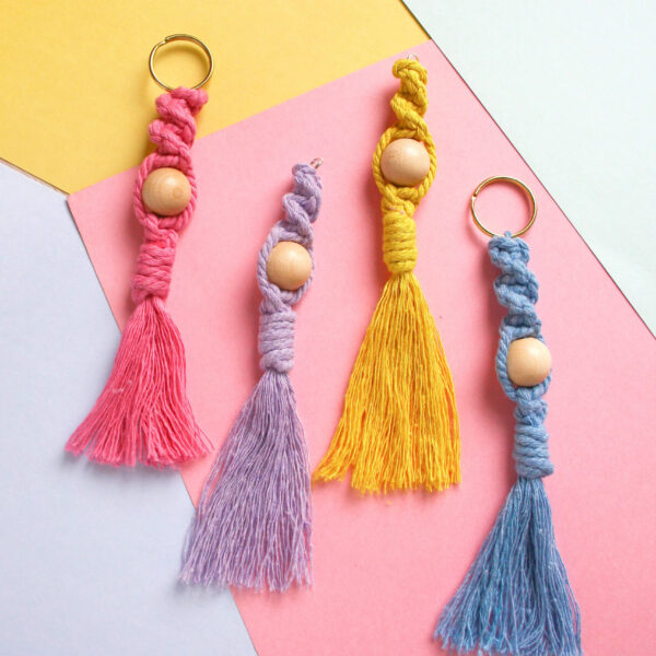 macrame keyring kit image, showing four finished macrame keyrings made from cotton cord and a wooden bead in pink, blue, lilac and yellow on a pastel background
