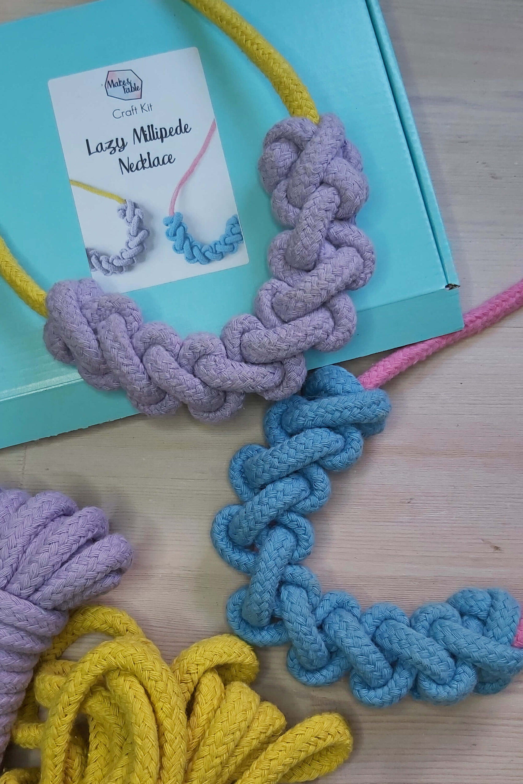 macrame rope necklace kit, showing a finished yellow necklace with lilac knotting, a pink necklace with blue knotting on an aqua blue box