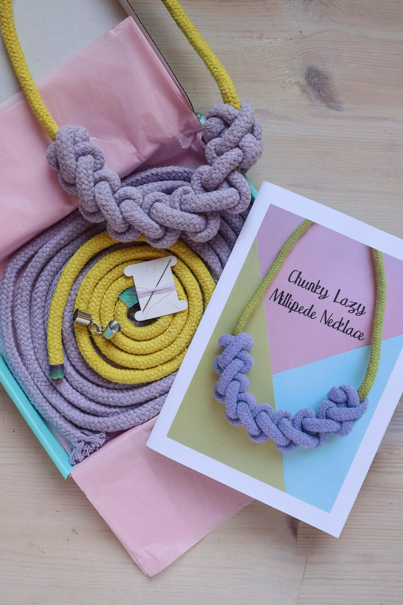 macrame rope necklace kit, showing a finished yellow necklace with lilac knotting, the full colour instructions and the materials all neatly coiled in their aqua blue box