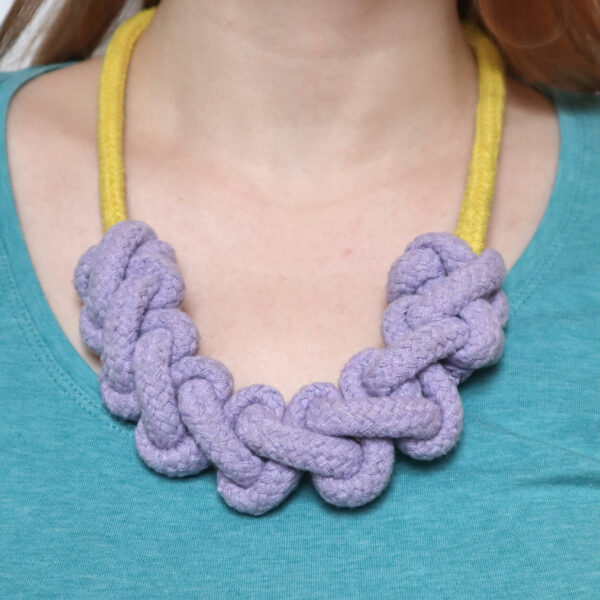 macrame rope necklace kit, showing a finished yellow necklace with lilac knotting, modelled on a white woman wearing a bright blue tshirt