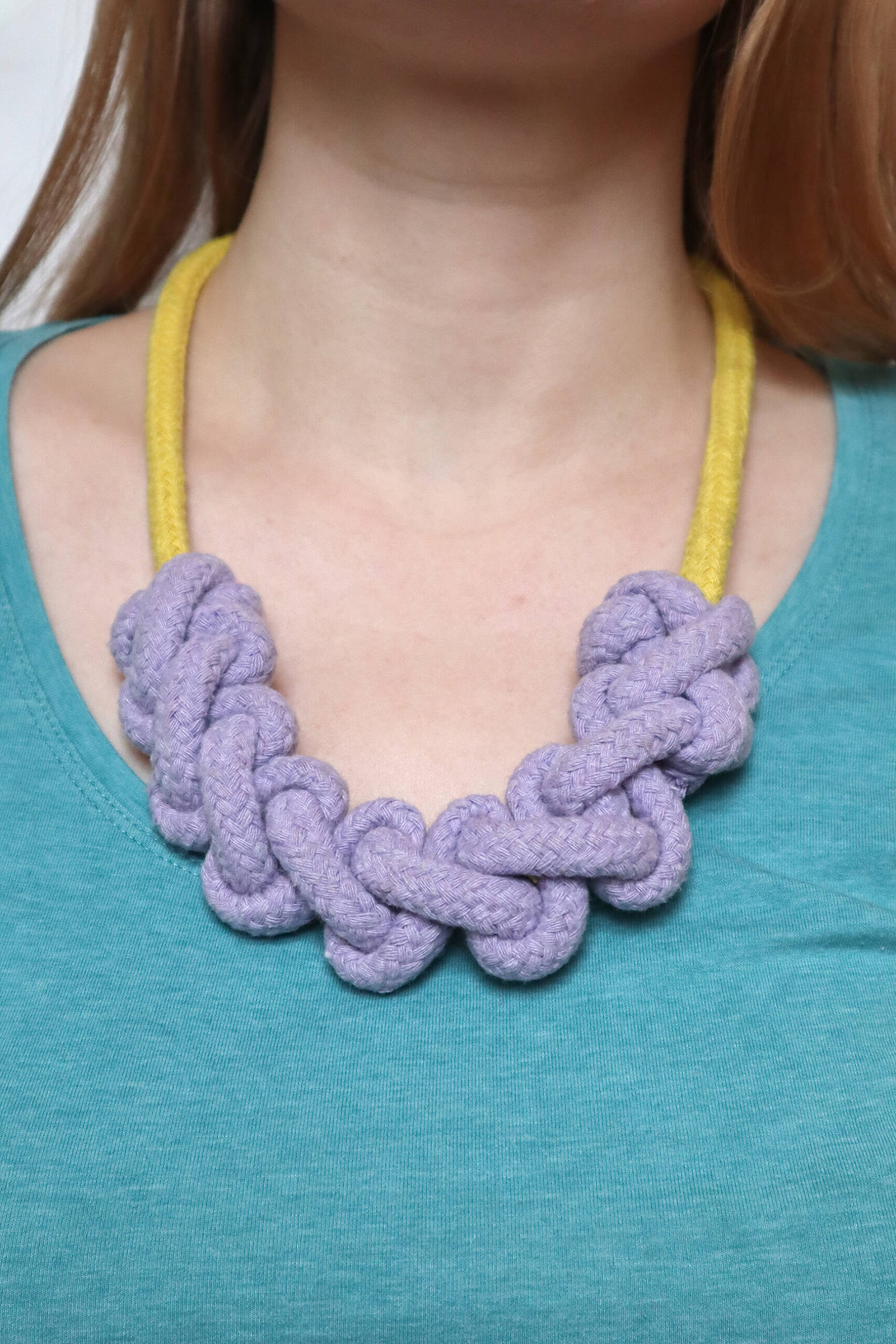 macrame rope necklace kit, showing a finished yellow necklace with lilac knotting, modelled on a white woman wearing a bright blue tshirt