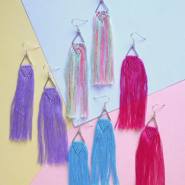 Macrame tassel earrings kit image show a finished pair of knotted earrings, with a triangle connector and long fringe in turquoise blue, fuchsia pink, pastel rainbow and mid purple