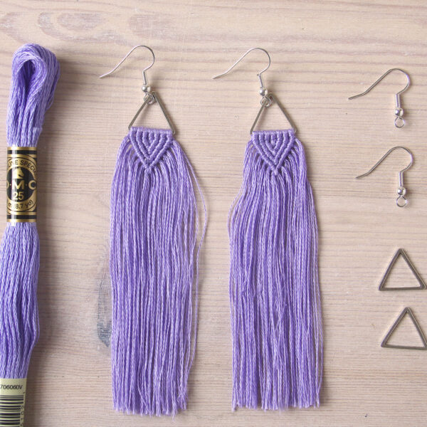 Macrame tassel earrings kit image show a finished pair of knotted earrings, with a triangle connector, silver plated fishhook style earrings and a fillskein of DMC embroidery thread
