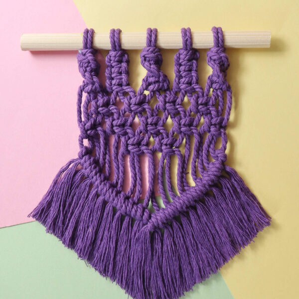 macrame wall hanging in purple on a pastel background