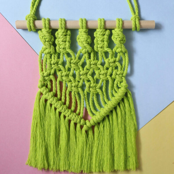 macrame wall hanging in neon green on a pastel background