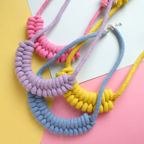 woven necklace kit finished items, featuring a lilac, pink, yellow and a blue macrame necklace all on a pastel background