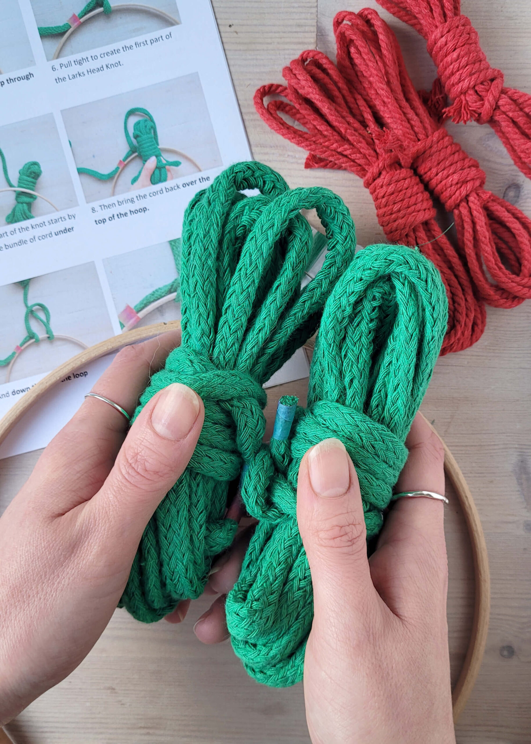 white hands holding green cotton cord with kit instructions and red cord in the background