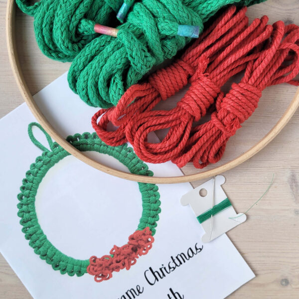 macrame Christmas wreath kit contents, showing instructions, wooden hoop, green and red cord and needle and thread