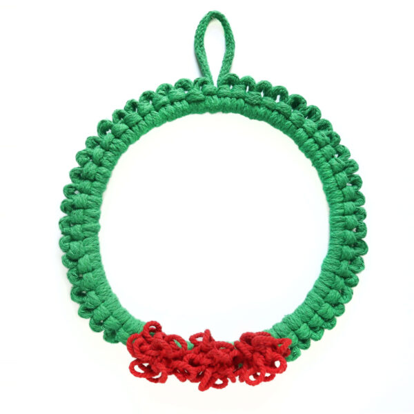 macrame Christmas wreath with green cord and bright red pom pom berries on a white wall