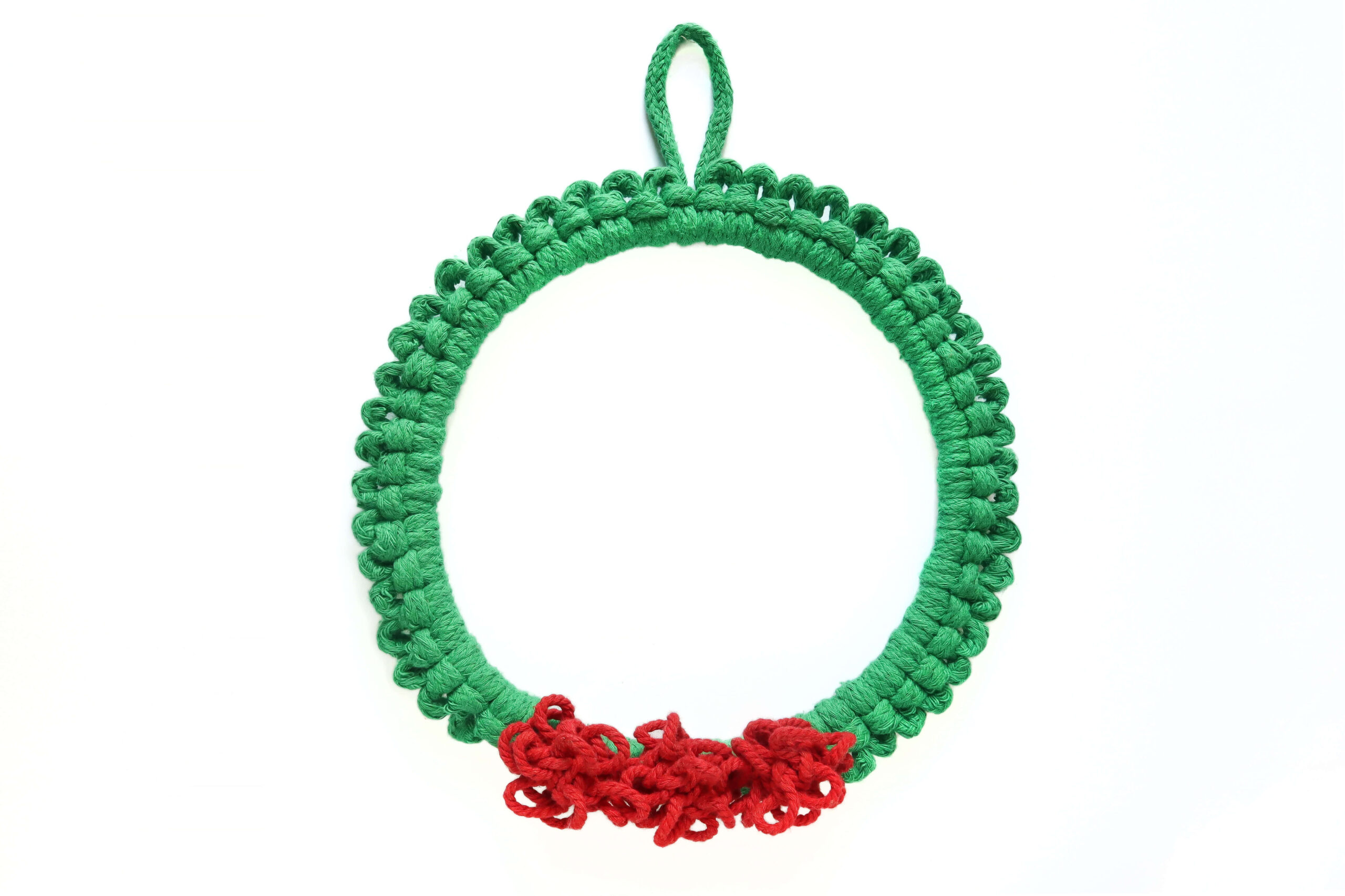 macrame Christmas wreath with green cord and bright red pom pom berries on a white wall
