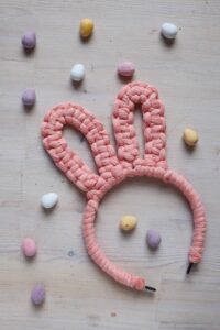 DIY macrame bunny ears headband in pink, surrounded by pastel colour chocolate eggs