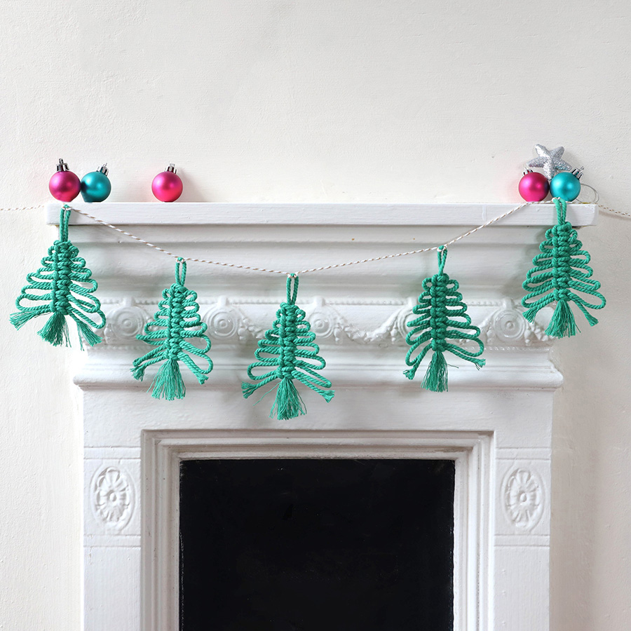 A garland of green macrame Christmas trees is hung above a fireplace