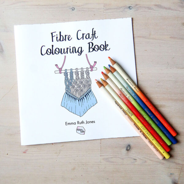 Fibre craft colouring book: a square format book with the image of a partially coloued in drawing of a macrame hanging on the cover. There are vintage colouring pencils lying on it.