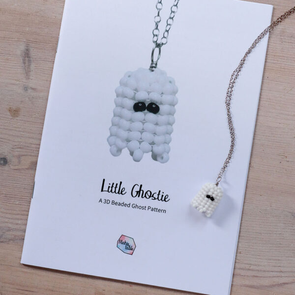 Beaded ghost pattern printed booklet on a wooden background, with a completed beaded ghost necklace