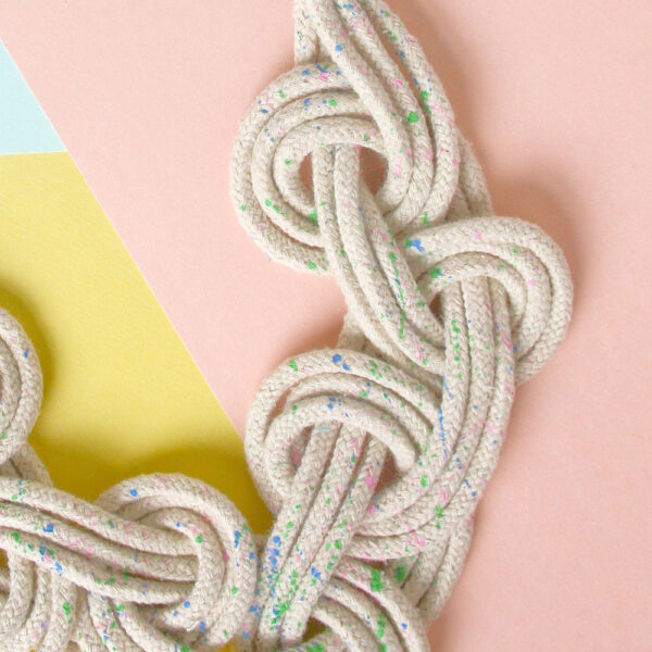 A Celtic style macrame necklace made in cream rope with colourful speckles cotton rope, on a pastel background
