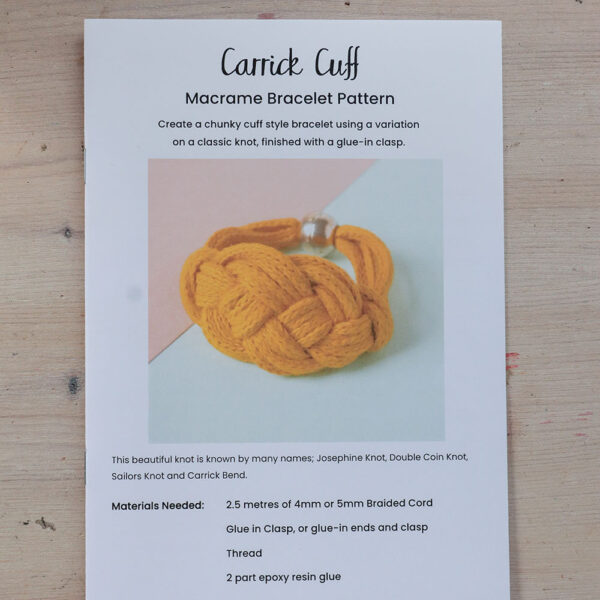 A printed pattern for the Carrick Cuff, a macrame bracelet pattern sits on a wooden background