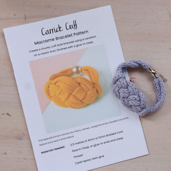 a printed pattern for hte Carrick Cuff, a macrame bracelet pattern sits on a wooden background with a completed purple example