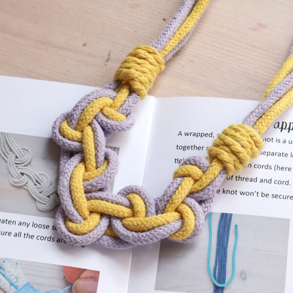 A Celtic style macrame necklace in lilac and yellow cotton rope, on a wooden table with the a5 printed pattern booklet