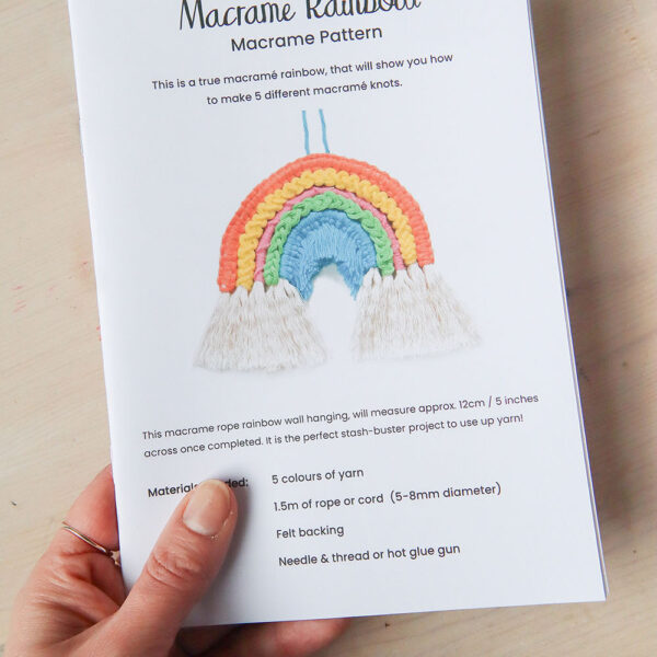 a hand holding the a5 printed instruction booklet for the macrame rainbow pattern