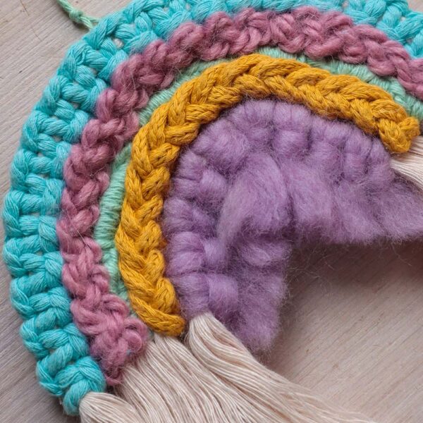 close up of a macrame rainbow made using different pastel yarns and cord, including cotton macrame cord, braid and wool roving