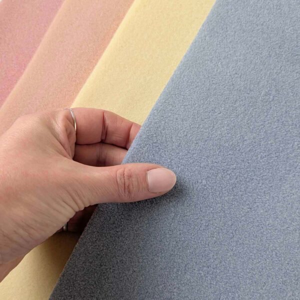 hand touching a blue beading mat. There is a yellow, peach and pink mat in the background
